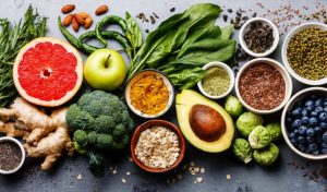 Eine Auswahl an frischem Obst, Gemüse und Samen, angeordnet auf einer grauen Oberfläche, darunter Grapefruit und Avocado.