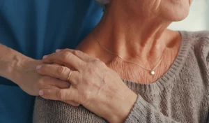 Eine Person legt sanft ihre Hand auf die Schulter einer älteren Frau und bietet ihr Trost und Unterstützung.