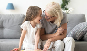 Lächelnde ältere Frau und junges Mädchen sitzen auf einer Couch, lachen und zeichnen zusammen.