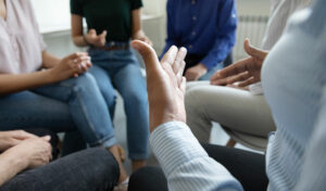 Menschen sitzen im Kreis und führen eine Gruppendiskussion. Dabei gestikulieren sie mit den Händen.