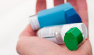 Eine Hand hält drei Asthmainhalatoren mit blauen, grünen und weißen Kappen.