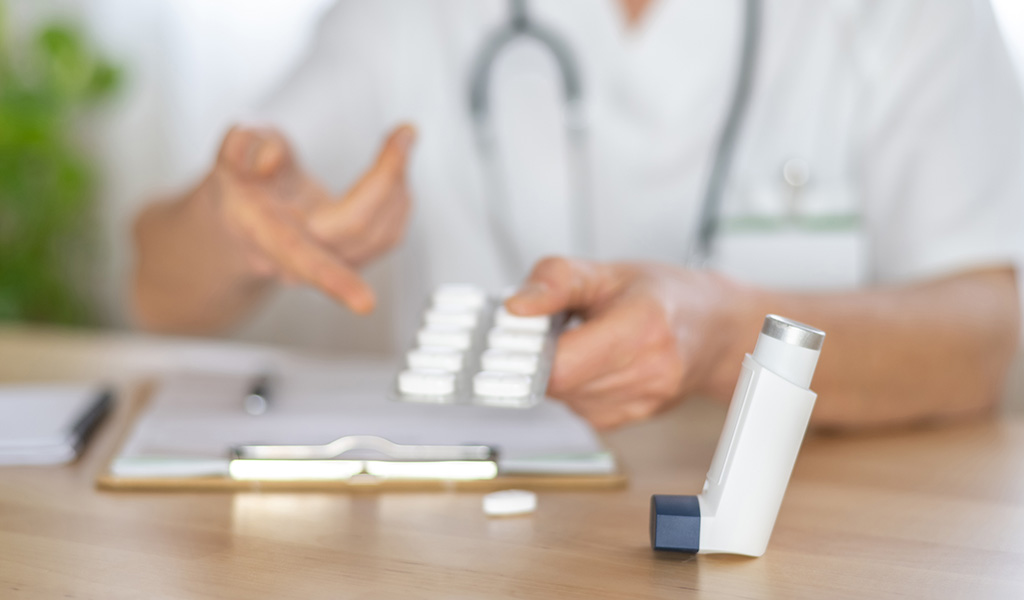 Arzt zeigt eine Blisterpackung mit Kortikosteroid-Pillen und einen Inhalator