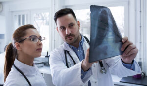 Zwei Ärzte untersuchen gemeinsam in einer hellen, modernen Arztpraxis eine Röntgenaufnahme des Brustkorbs.