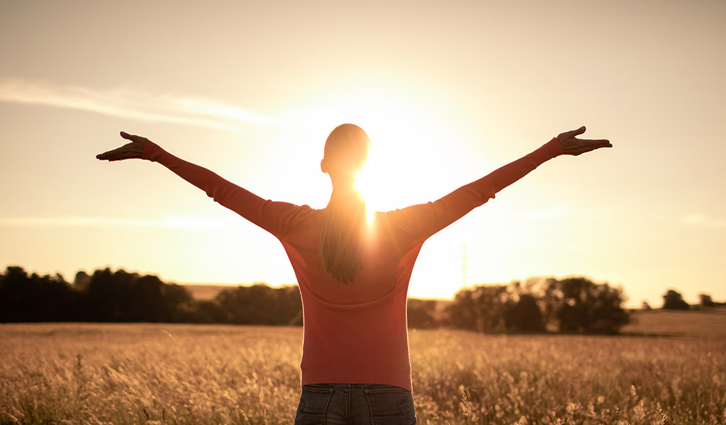 Junge Frau auf der Wiese, die die Schönheit und Wärme der Sonne aufnimmt