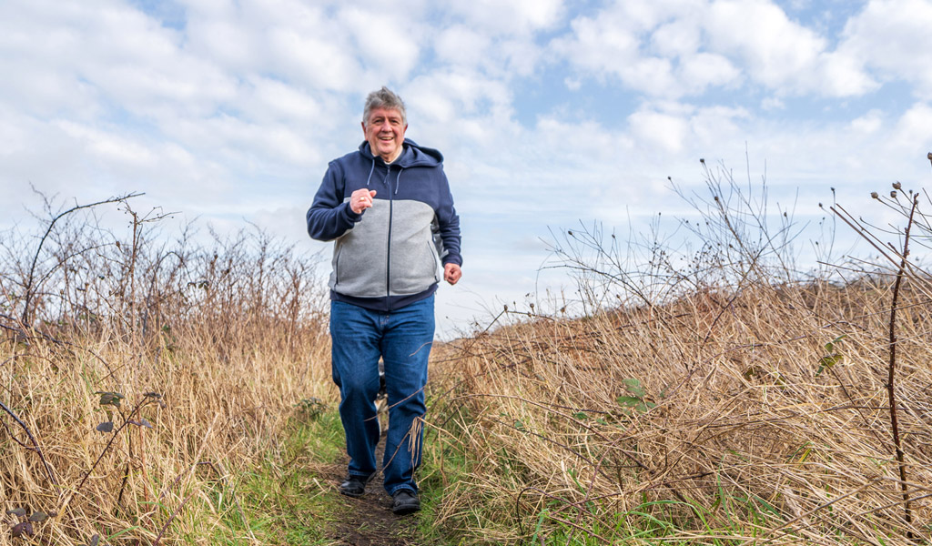Älterer Herr im Sportoutfit joggt auf Grünland