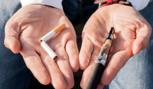 Zwei Hände, die in der einen Hand eine zerbrochene Zigarette und in der anderen einen Vape-Pen halten, symbolisieren das Aufhören mit dem Rauchen.
