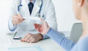 Ein Arzt übergibt einem Patienten in einer Arztpraxis über den Schreibtisch hinweg ein Rezept oder ein Dokument.