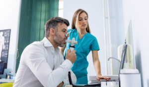 Ein Mann führt mit einem Spirometer einen Atemtest durch, während ein Mitarbeiter des Gesundheitswesens die Ergebnisse auf einem Computer überwacht.