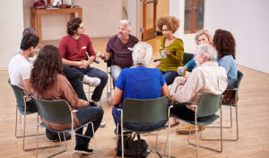 Eine bunt gemischte Gruppe von Menschen sitzt in einem hellen Raum im Kreis und diskutiert.