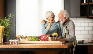 Lächelndes älteres Paar kocht zusammen in einer modernen Küche und teilt einen freudigen Moment an der Theke.