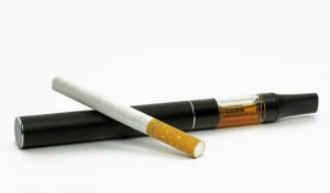 Eine herkömmliche Zigarette und ein schwarzer Vape-Pen sind nebeneinander auf einem weißen Hintergrund platziert.