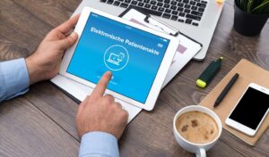 Person, die ein Tablet mit Elektronischen Patientenakten auf dem Bildschirm an einem Schreibtisch mit Kaffee und Büroartikeln verwendet.