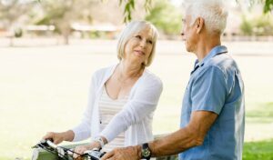 Eine ältere Frau mit einem Fahrrad lächelt und unterhält sich an einem sonnigen Tag draußen in einem Park mit einem älteren Mann.