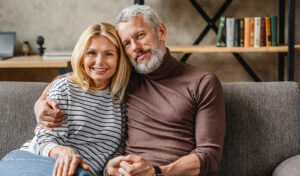Lächelndes Paar sitzt auf einer Couch und umarmt sich in einem gemütlichen Wohnzimmer.