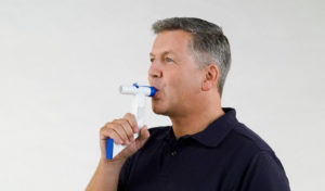 Mann in einem dunklen Poloshirt benutzt vor einem schlichten Hintergrund ein tragbares medizinisches Beatmungsgerät.