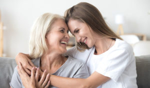 Zwei Frauen lächeln und umarmen sich, während sie auf einem Sofa sitzen und einen glücklichen und liebevollen Moment teilen.