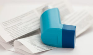 Ein blauer Asthma-Inhalator liegt auf gefalteten Gebrauchsanweisungen.