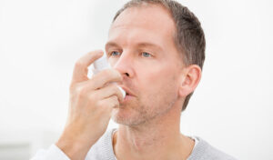 Ein Mann verwendet ein Nasenspray und hält die Flasche in einem hellen Innenraum an sein Nasenloch.