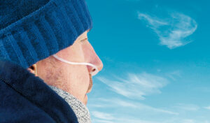 Mann in Winterkleidung mit Sauerstoffschlauch in der Nase blickt in einen blauen Himmel mit dünnen Wolken.