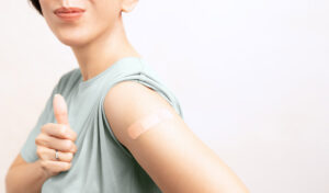 Frau zeigt nach einer Impfung den Daumen nach oben und einen Verband an ihrem Oberarm.