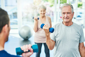 Ältere Erwachsene trainieren mit Hanteln in einem hellen Fitnessstudio, lächeln und bleiben gemeinsam aktiv.